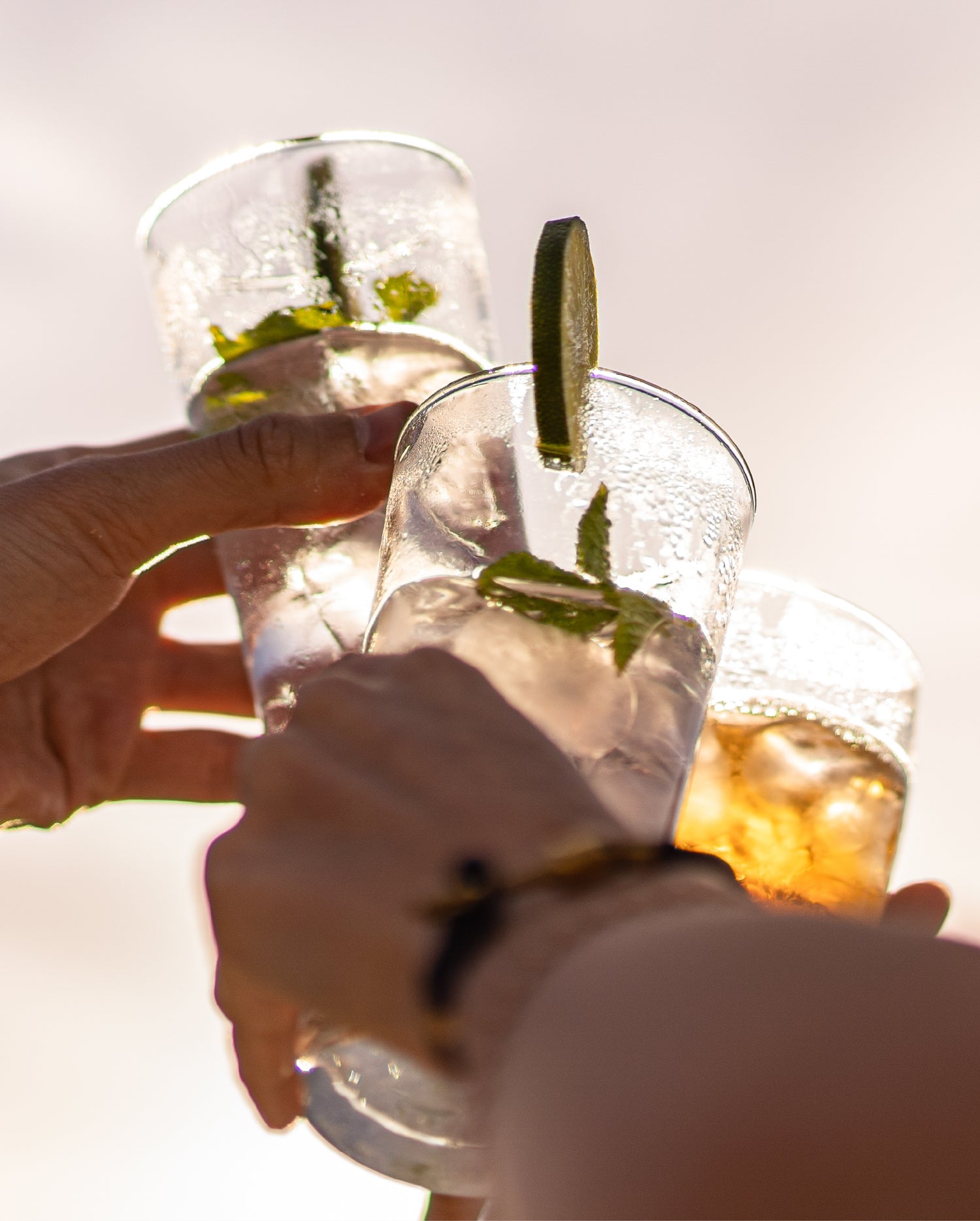 Three hands raising glasses of different flavors of Sparkling Elixir in a toast.