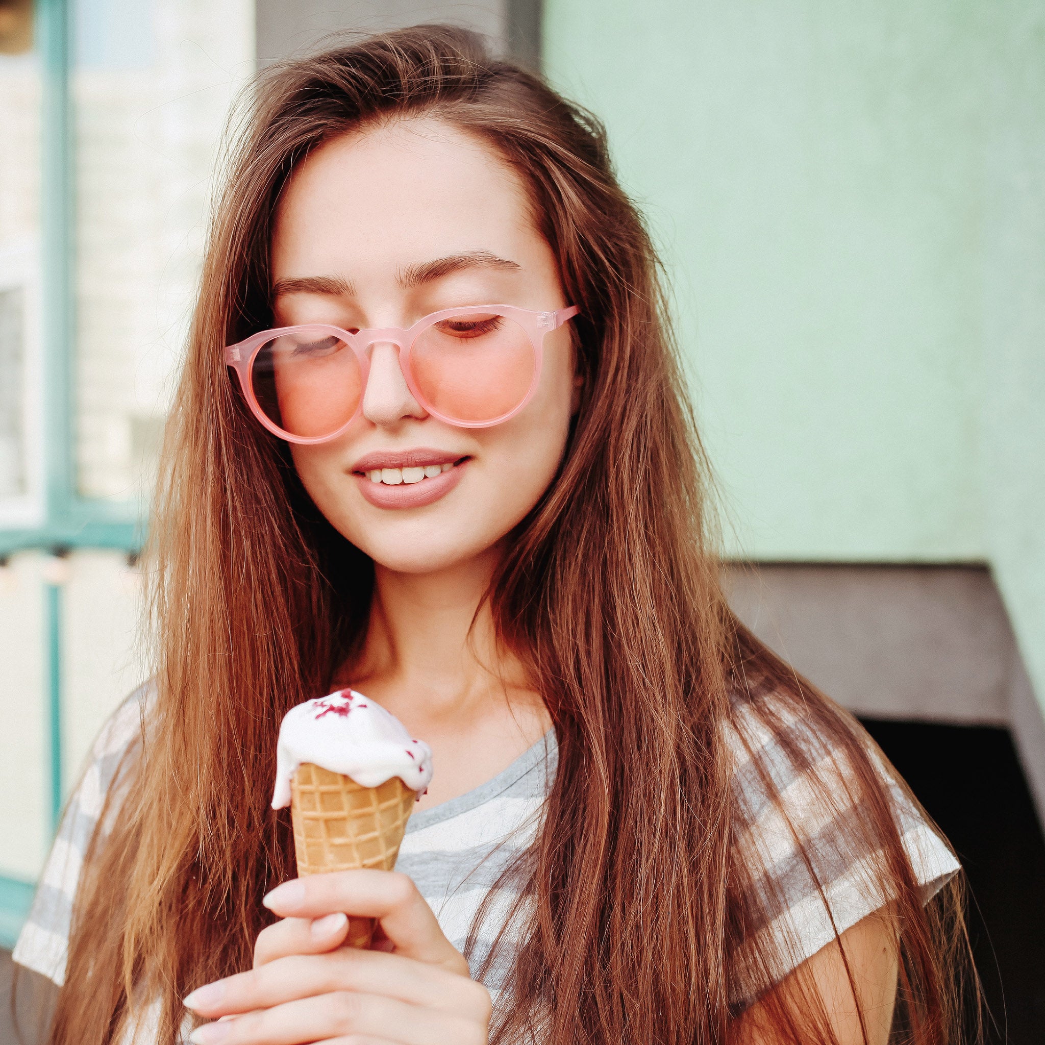 Young woman with pink framed glasses and a striped shirt, holding an ice cream cone.